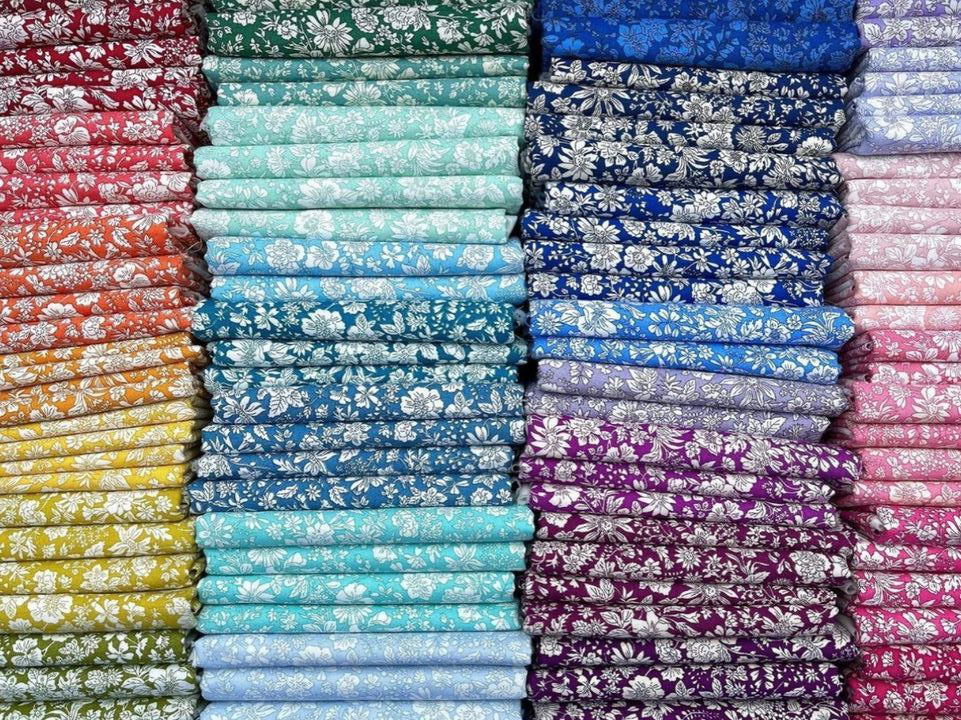 A dense, colorful arrangement of folded patterned fabric rolls stacked horizontally, showing a wide variety of colors and floral motifs.