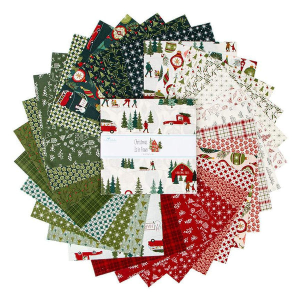 Image of Christmas Is in Town 10&quot; Stacker by Riley Blake Designs. Features a cream fabric with trees, cabins, people, and snow. Cute Little Fabric Shop