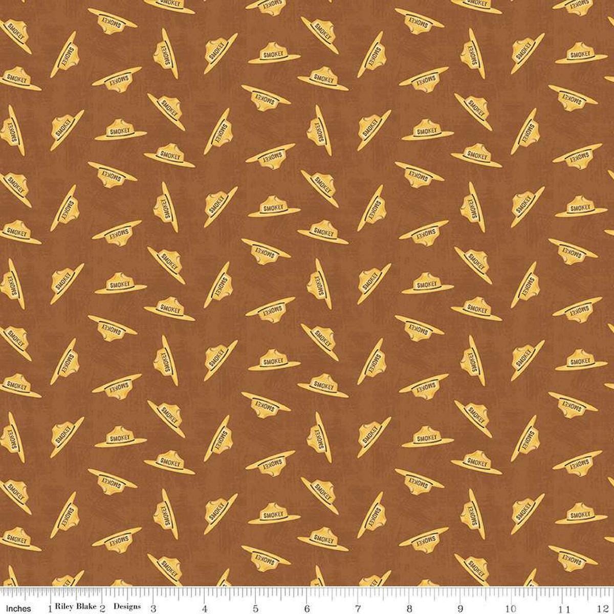 Image of the Friends of Smokey Bear Hat Toss Sienna quilting cotton fabric. Features hats on a brown background. Cute Little Fabric Shop