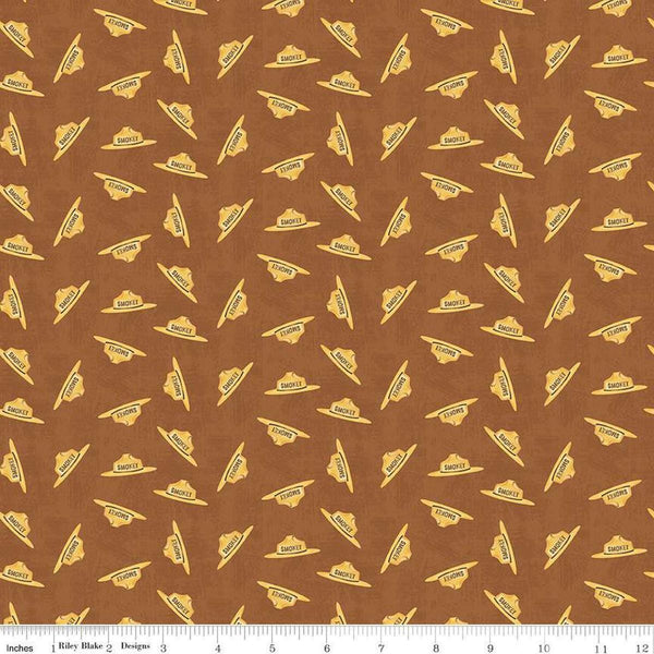 Image of the Friends of Smokey Bear Hat Toss Sienna quilting cotton fabric. Features hats on a brown background. Cute Little Fabric Shop