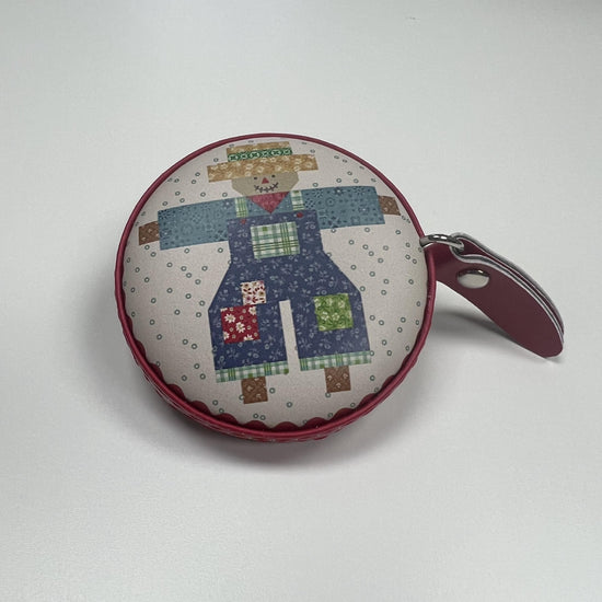 A round, colorful pouch or coin purse with a patchwork design depicting a scarecrow or scarecrow-like figure.
