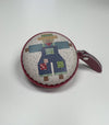 A round, colorful pouch or coin purse with a patchwork design depicting a scarecrow or scarecrow-like figure.