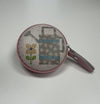 A round, pink coin purse with a floral pattern and a watering can design printed on it.
